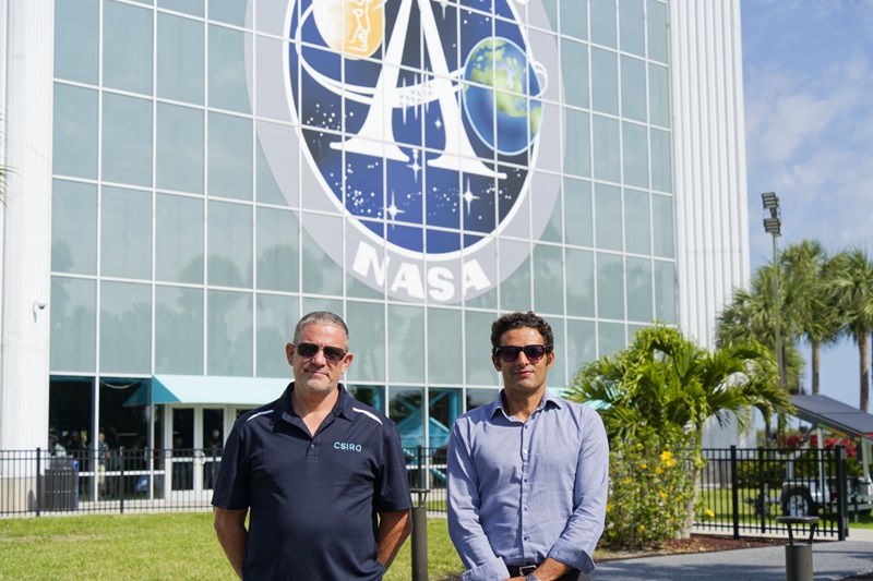 Two men standing in front of the NASA logo on a building facade. 