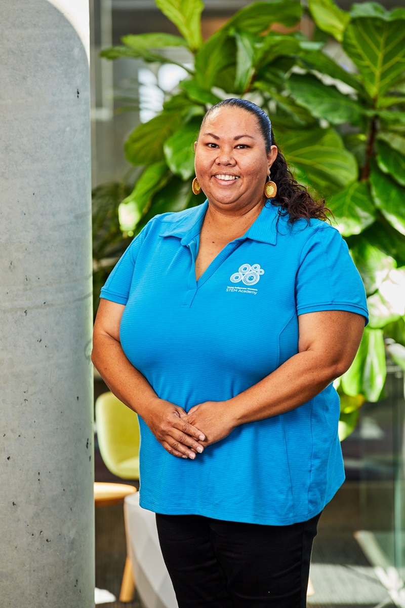 Woman standing in blue shirt in front of a tall plant.