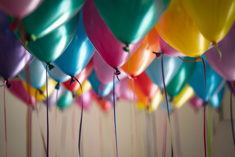 Inflated balloons of all different colours with strings attached are floating in the air 