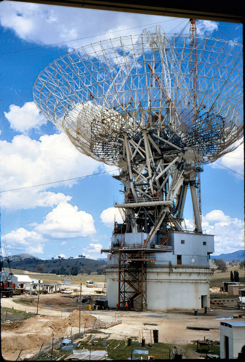 An astronomy antenna under construction with hills and a cloudy sky in the background.