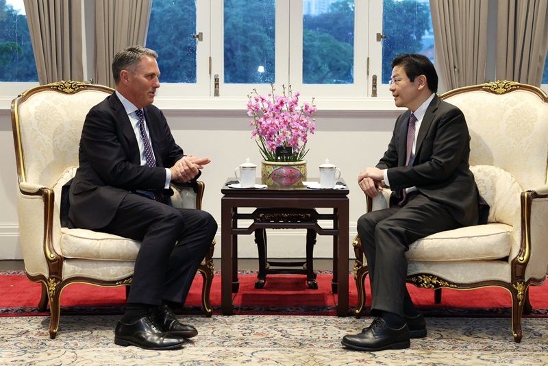 Richard Marles on the left in an armchair facing Lawrence Wong on the right in an armchair. A side table in between with pick orchids.