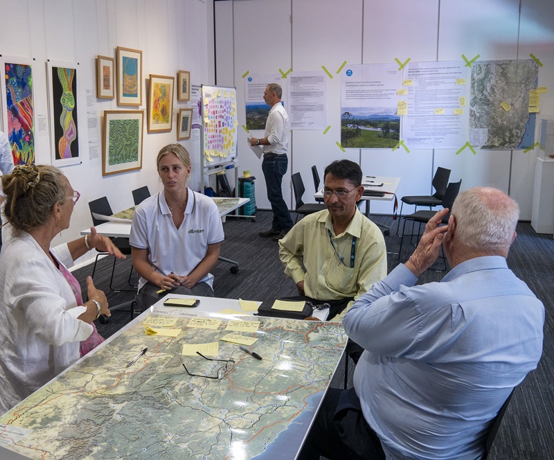 Jai Vaze and a consultant at a table talking to residents. Maps and information is attached to the walls in the room.