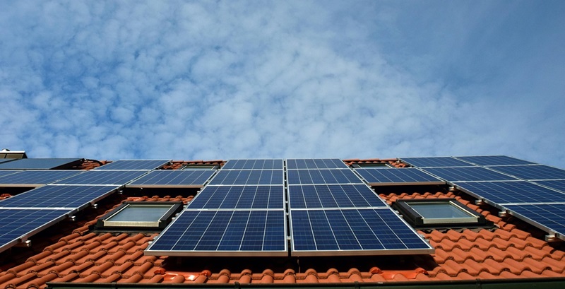 solar panels on a red tiled roof against a blue sky with clouds
