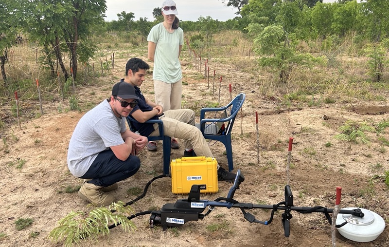 Three people in field around metal detector-like device