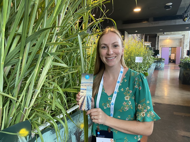 Dr Sarah Hartman standing among tall plants at an agricultural innovation event, holding CSIRO materials.