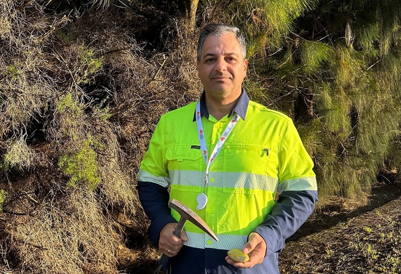 Man in hi-vis holding a rock and mining pick.