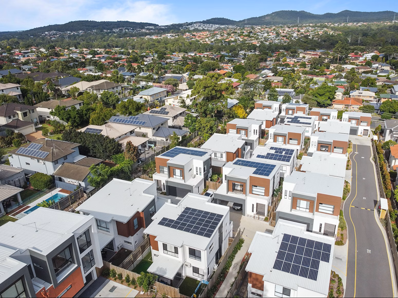 Edge of a city showing roof tops with solar panels and hills in the distance