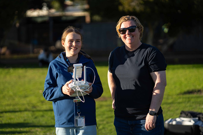 CSIRO Chief Remote Pilot Amanda Meys stands next to a female future shaper who holds the controls to a drone.png