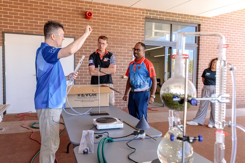 Three people standing around a basic chemistry set up for oil distillation 