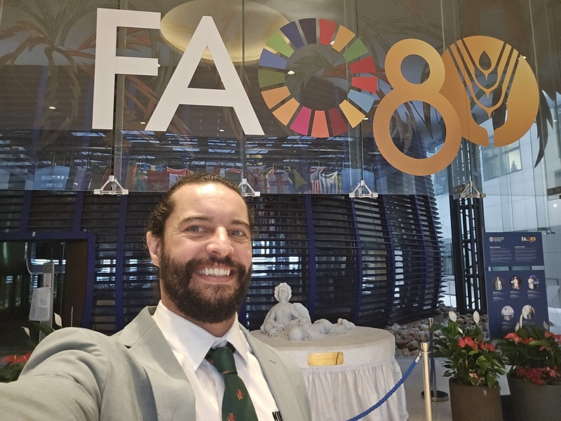 Dr Jonathan Richetti smiling in front of the FAO logo inside the Food and Agriculture Organization headquarters.