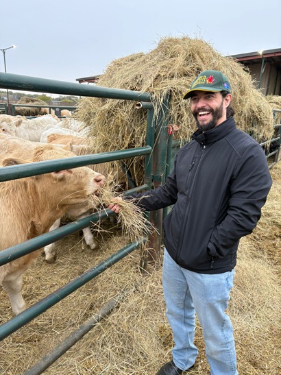 Dr Jonathan Richetti smiling as he feeds hay to cattle through a fence on a farm.