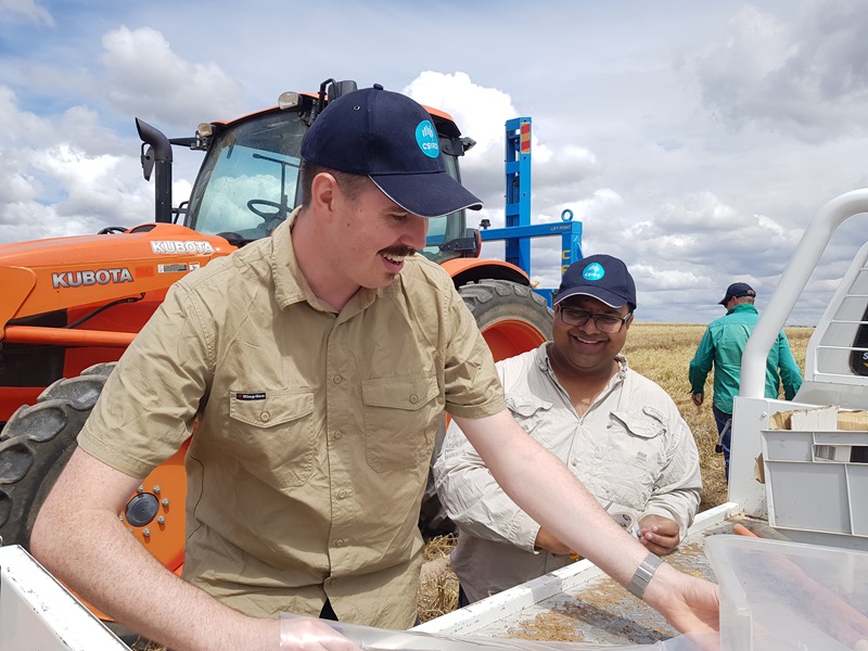 Two men smiling while standong by the tray of a ute in a crop field.
