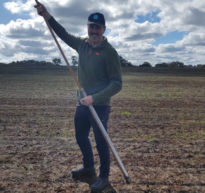 A man stands in a field whilst holding a pole.