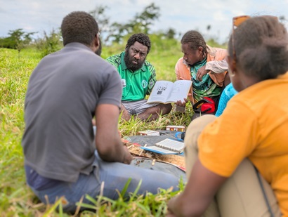 A group of people in the Pacific Islands sit in a circle, whilst studying soil samples.