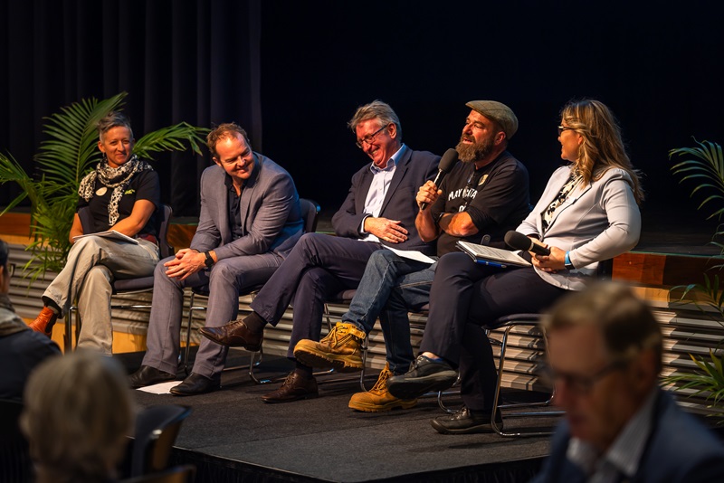 A panel of five speakers sit on stage discussing circular-economy opportunities; one panellist holds a microphone while the others listen and smile.
