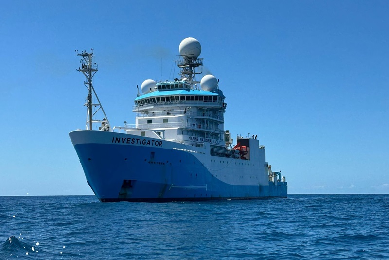 A blue and white ship on the open ocean viewed from nearby on the surface of the ocean.