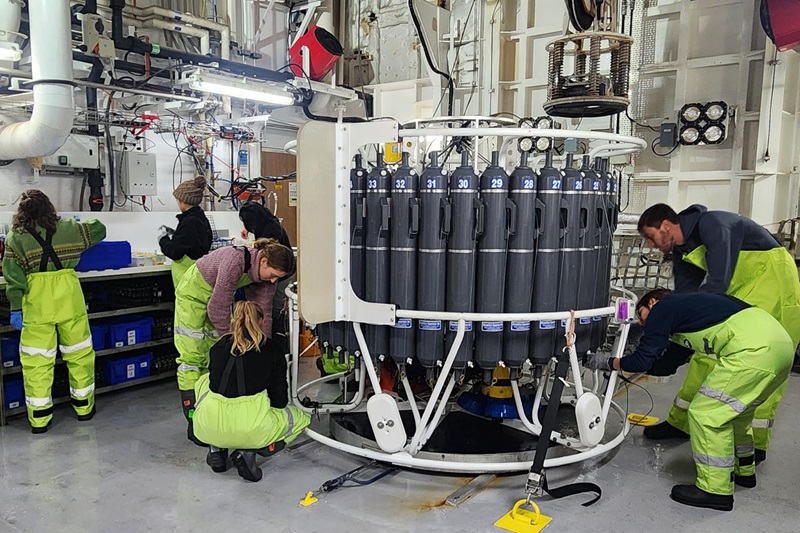 A group of people work around a large circular piece of scientific equipment in a laboratory.