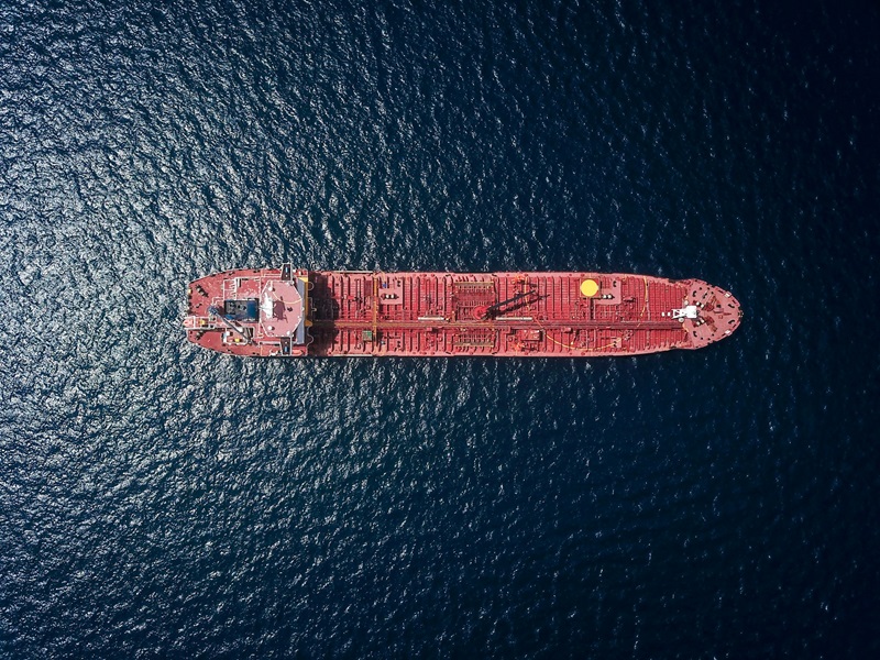 Aerial view of a large red cargo ship on deep blue open ocean, photographed directly from above.
