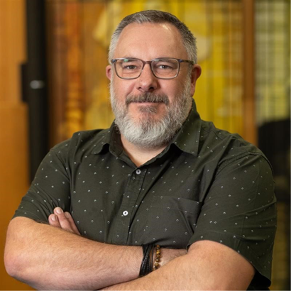 Corporate headshot of a man wearing glasses in a grey collared shirt.