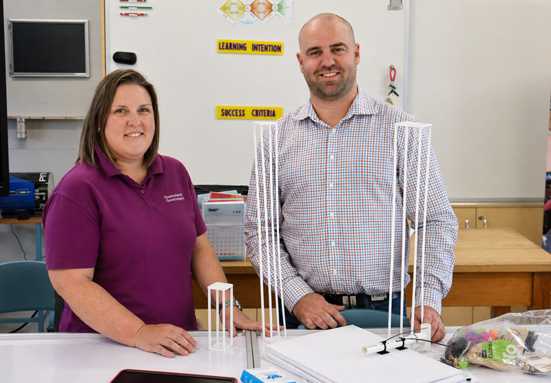 A woman and man standing in front of tower structures positioned on a table in a classroom setting