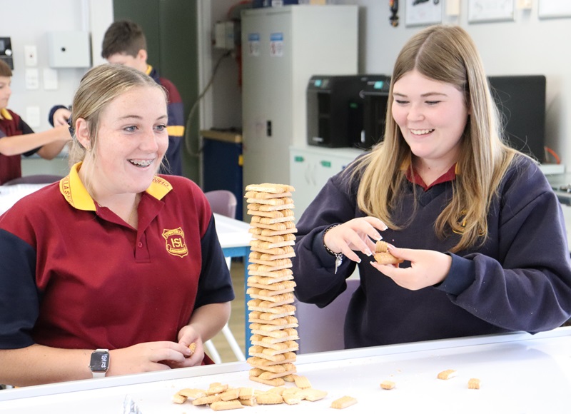 Two students smiling as they look at a tower made out of biscuits
