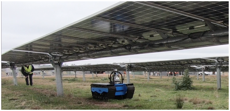 Robot underneath solar panels driving on grass. 