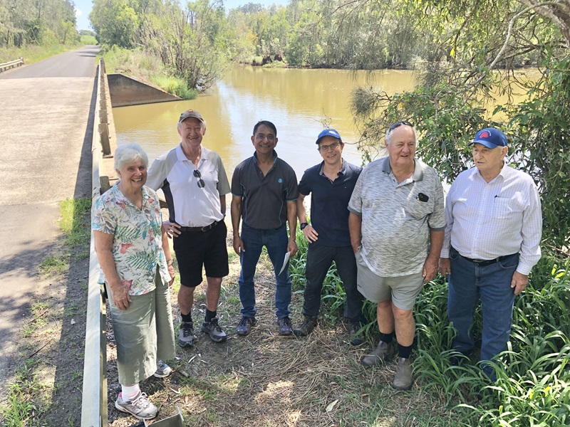 A group photo of six people with a river behind and a bridge to the left