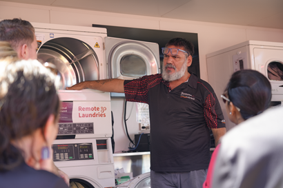 Inside a remote laundry with a person standing beside a washing machine in discussion with a group of people
