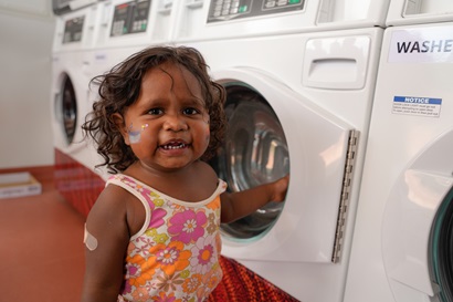 Young girl smiling, beside a row of washing machines