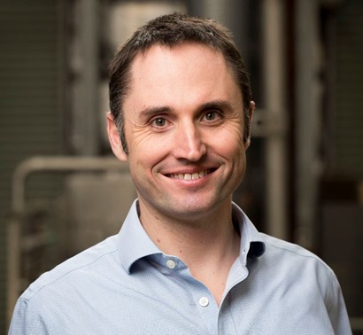 Man with collared shirt smiles at camera in a lab background
