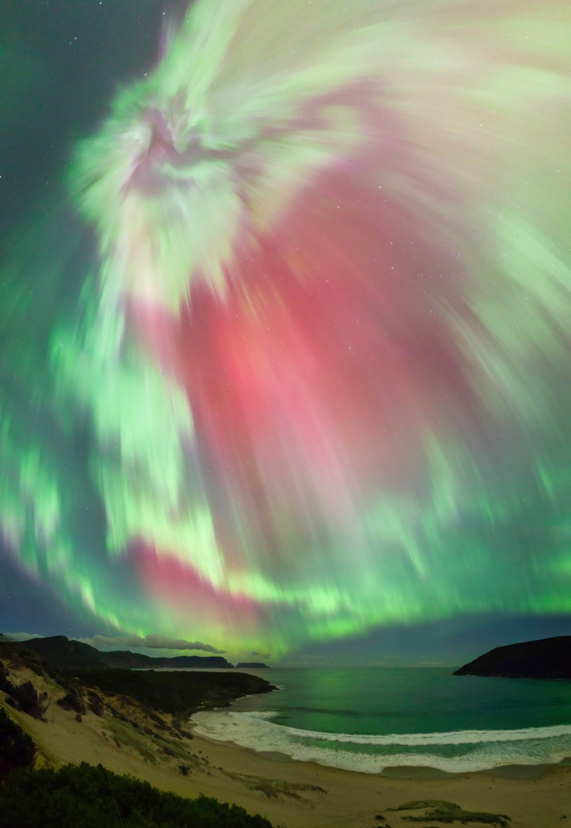 A beach sits below a sky filled with green and pink light.
