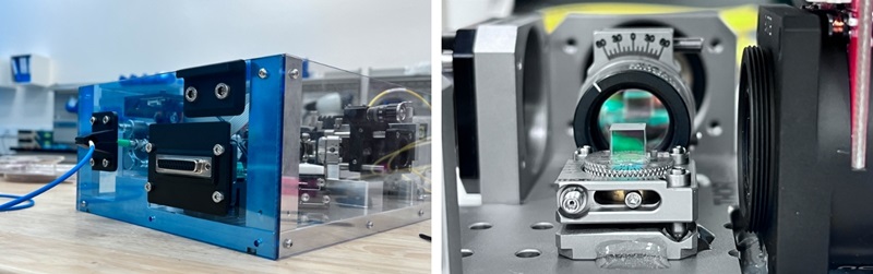 image of a blue-faced shiny box with complex looking parts attached on the left and a glass cube in front of lenses on the right.