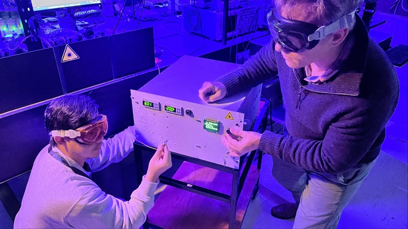 CSIRO Technical Lead, Dr Matt Broome and colleague Minh Nguyen working on the Quantum Light Source wearing protective glasses in a room bathed in purple light