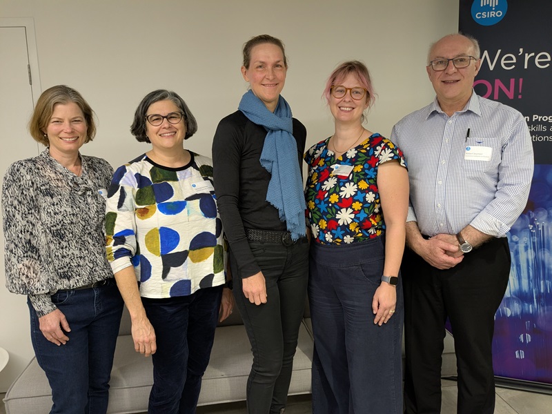 Five CSIRO staff stand smiling for a group photo in front of a banner reading 