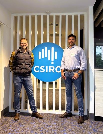 Two men stand either side of a large blue CSIRO logo in an office foyer.