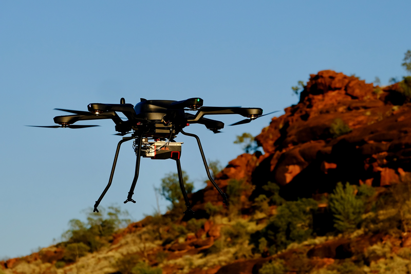 A drone with red rocky outcrop in the background against a blue sky
