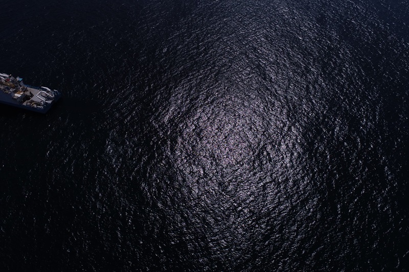 Drone photo of a circle of sun reflecting off the surface of a dark ocean
