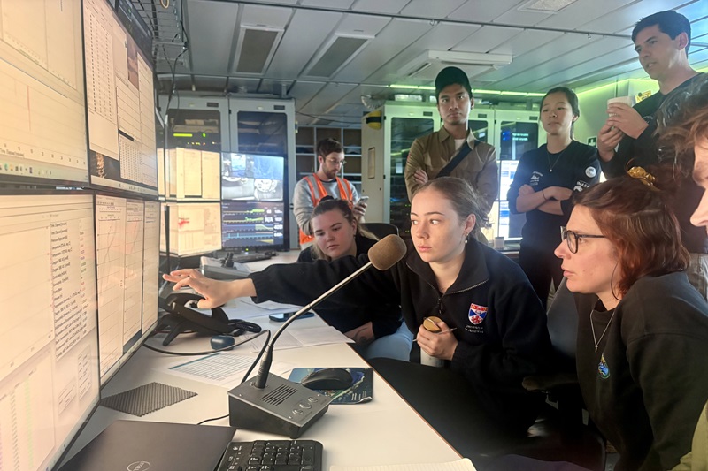 A group of people staring at computer screens while one person points at a screen.