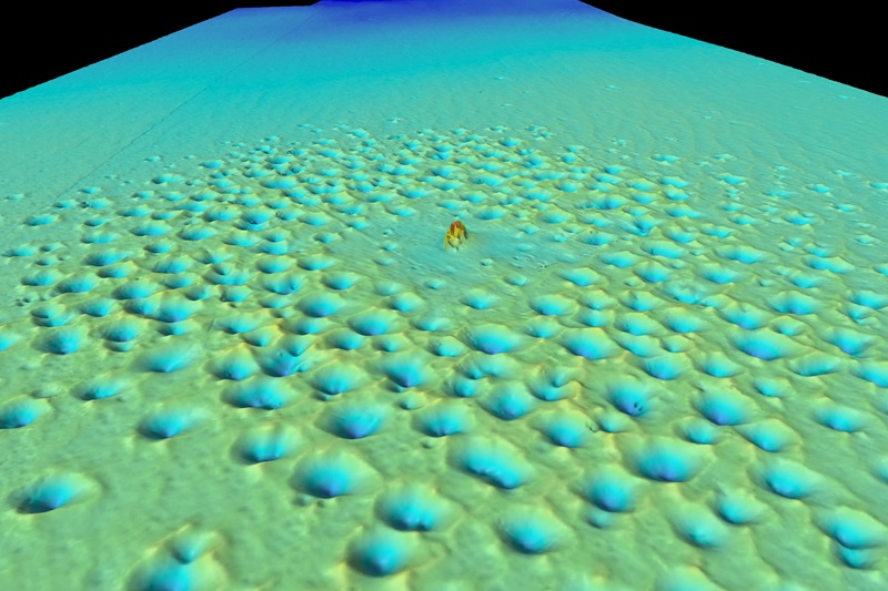 A colourful image of the seafloor with a shipwreck shown in orange in the middle and a circle of holes in the seafloor around it.
