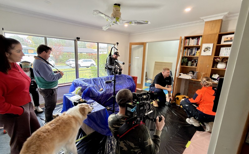 A film crew inside a home with someone interviewing an expert, being filmed, with a dog watching on.