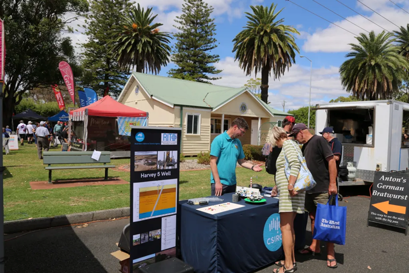 People at a small stand with the CSIRO logo on the tablecloth and a banner next to the stand, in a parkground setting