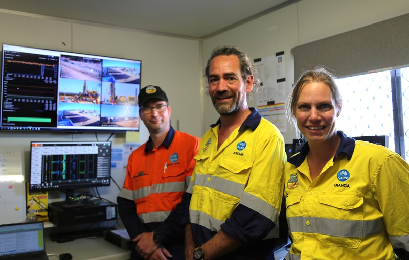 Three people in high viz uniforms in a small onsite building with monitors on the wall