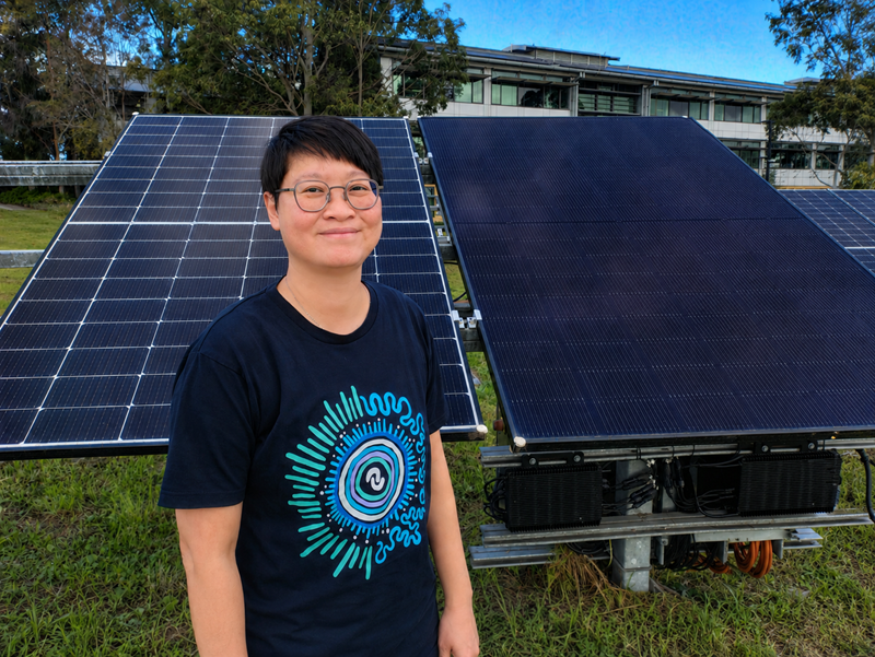 Woman stands on grass in front of solar panels in outdoor facility. 