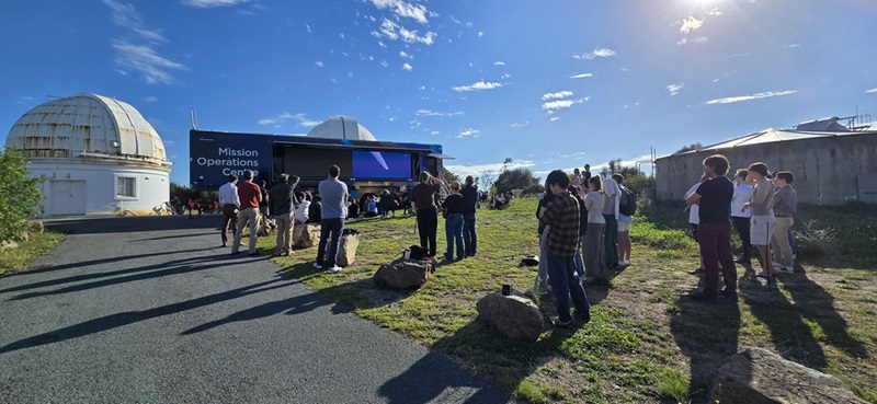 People standing watching screens on outside of sapce truck