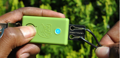Hands holding a green instrument with a chameleon and the letters VIA embossed on the rectangular contraption