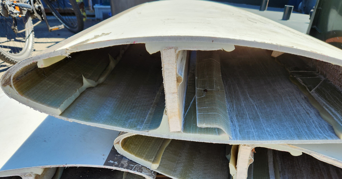 Cross-sections of wind turbine blades stacked on a wooden pallet, showing internal fibreglass structure.
