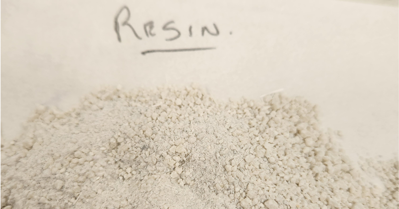 A pile of granular recovered resin on paper, with a handwritten label reading "resin".