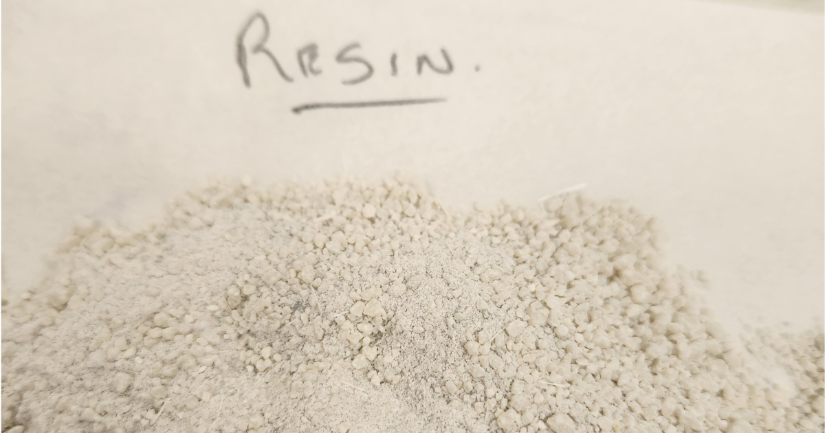 A pile of granular recovered resin on paper, with a handwritten label reading "resin".