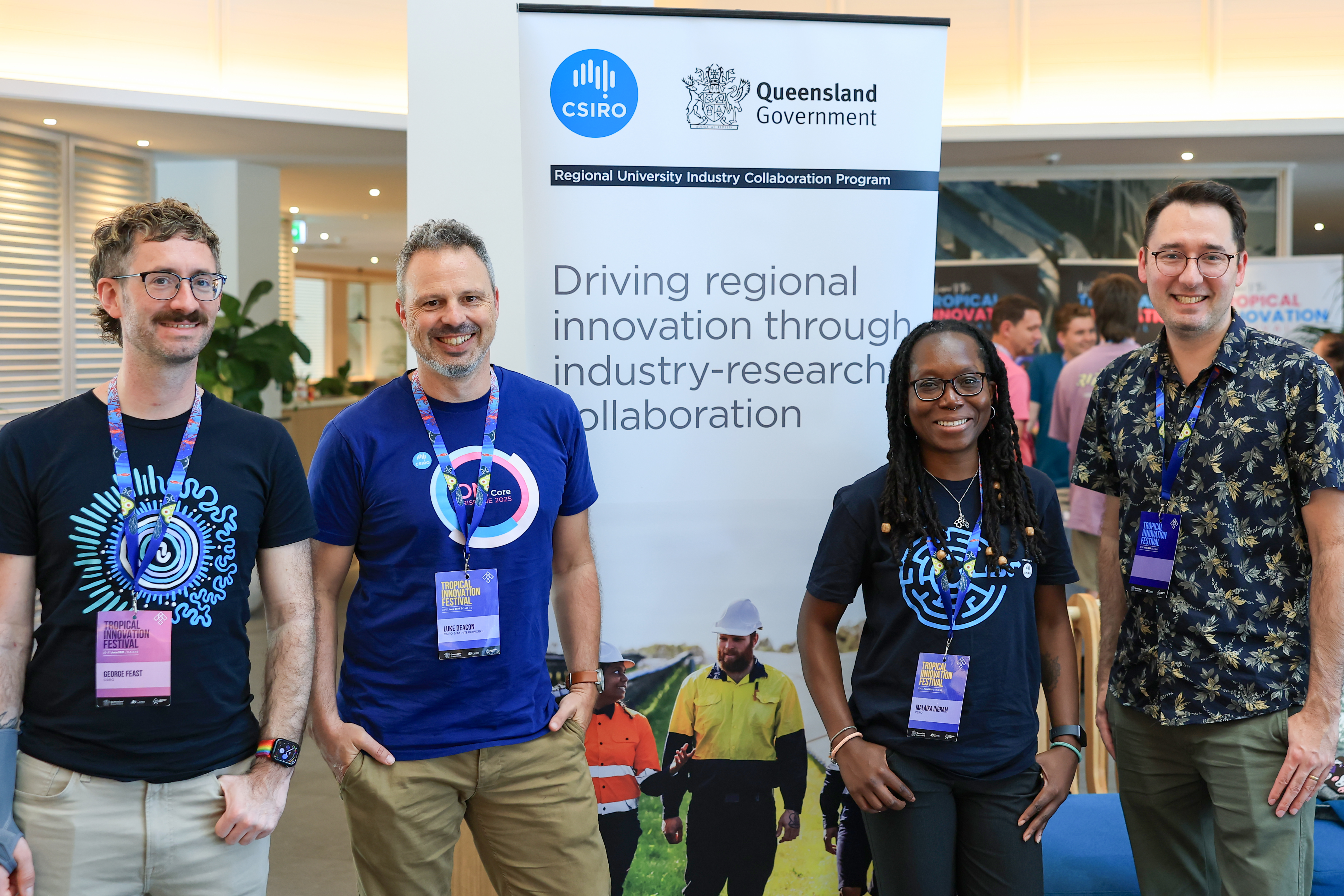 Four people standing infront of a Regional University Industry Collaboration Program pull-up banner