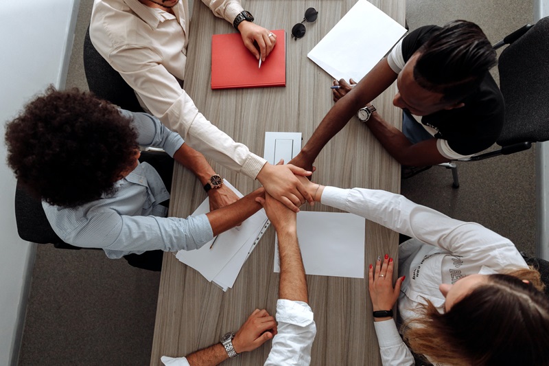 A group of people all clasping hands over a table to symbolise collaboration.